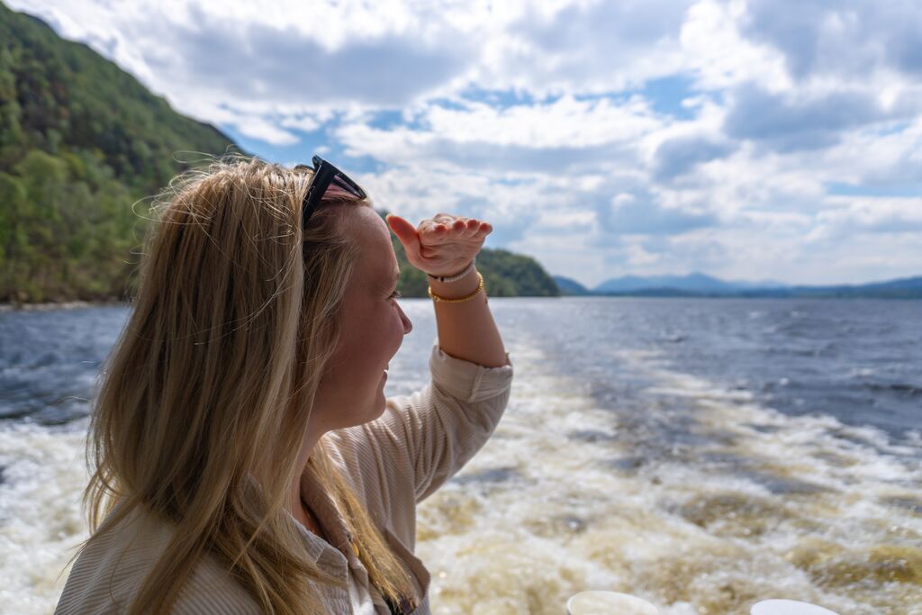 Young woman looking for Loch Ness monster on boat cruise
