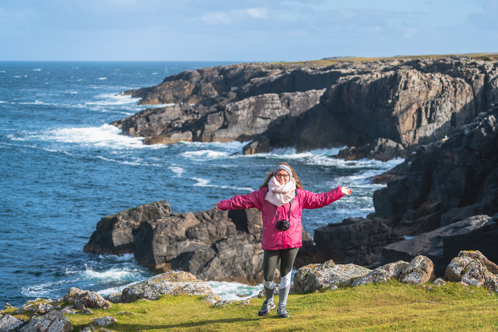 Young woman standing before the rugged coast on a sunny day in the Outer Hebrides
