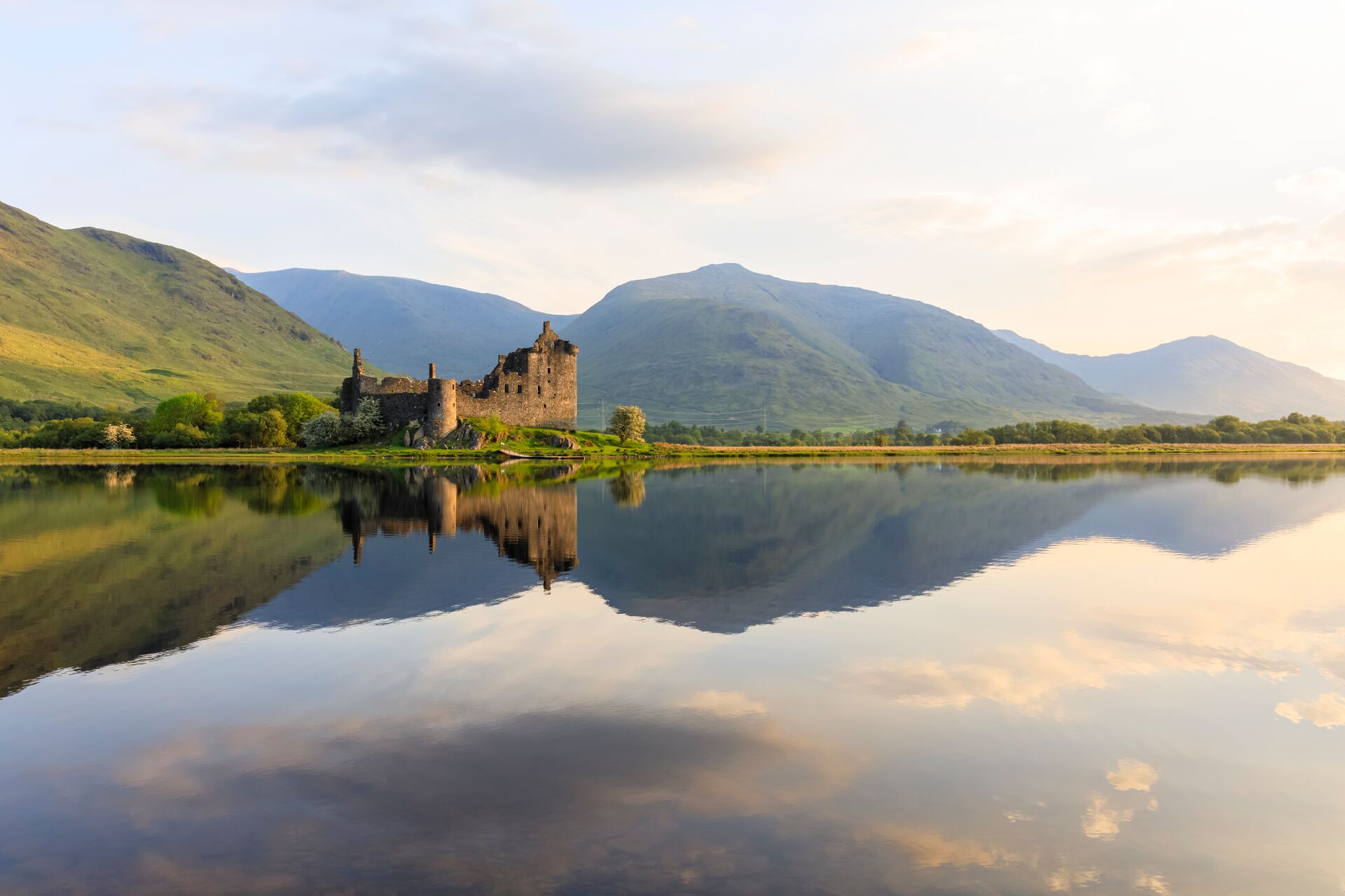 Kilchurn Castle bathed in afternoon sun, its ruins mirrored in the still, reflective waters of Loch Awe